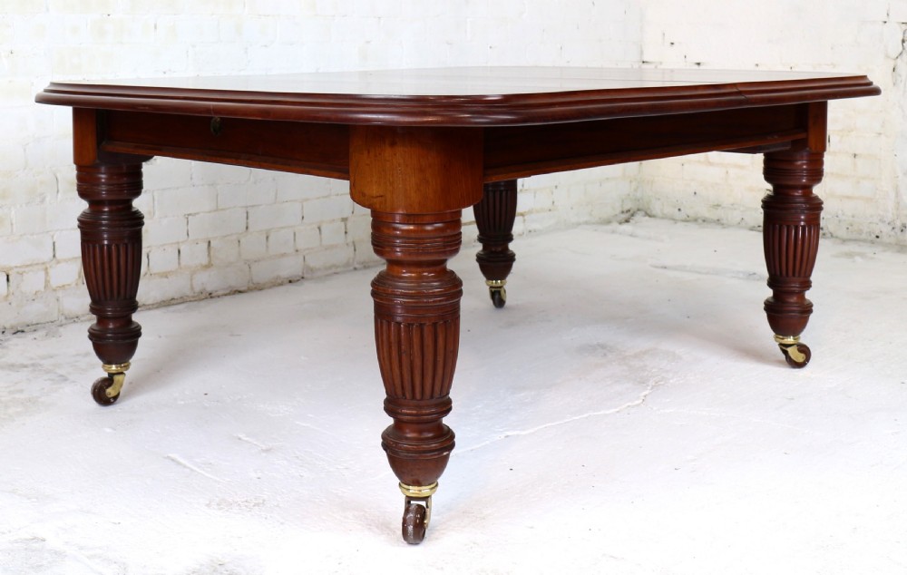 A large Victorian mahogany extending dining table with rounded corners, three insertion leaves, and carved fluted turned legs resting on brass castors. View XX