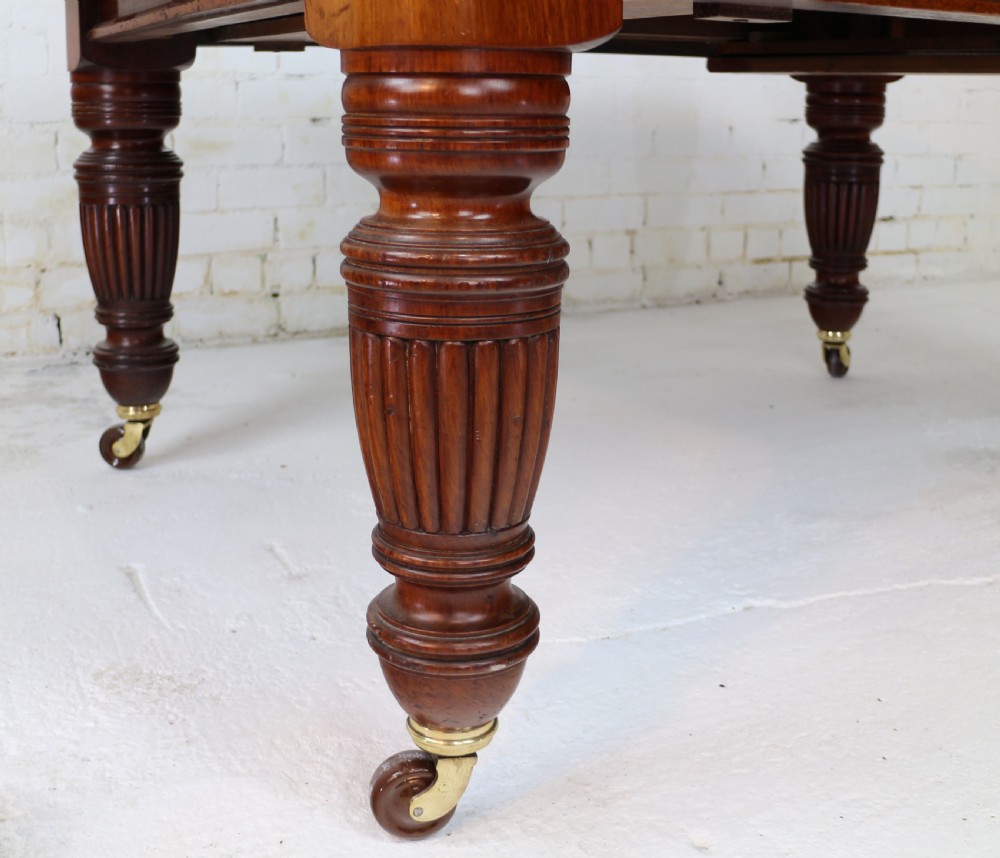 A large Victorian mahogany extending dining table with rounded corners, three insertion leaves, and carved fluted turned legs resting on brass castors. View XXI