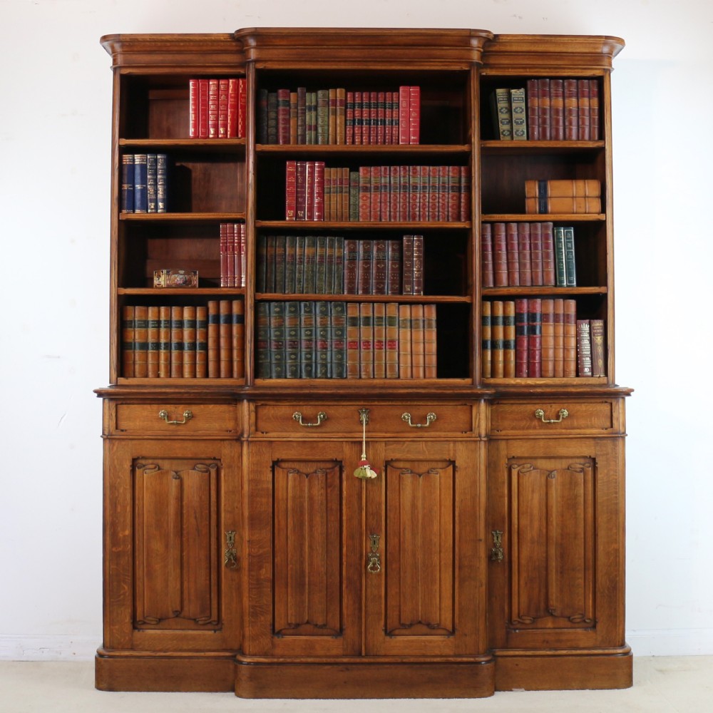 A large Victorian Gothic oak breakfront bookcase featuring open upper shelves filled with books and carved lower cupboard doors. View II