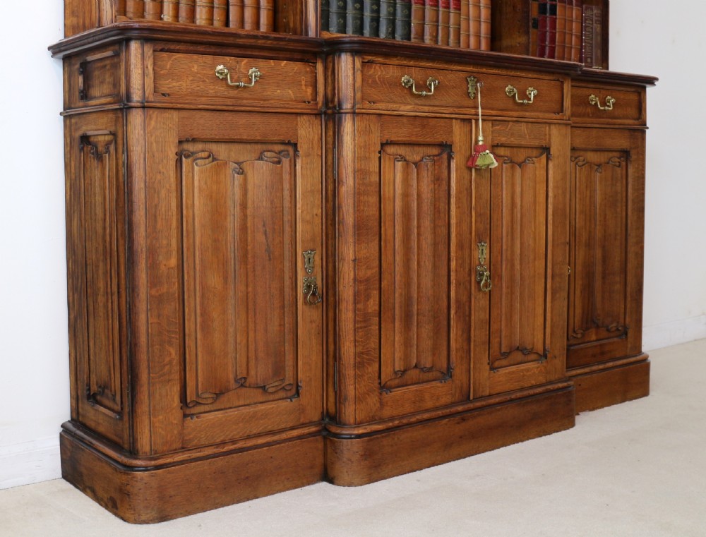 A large Victorian Gothic oak breakfront bookcase featuring open upper shelves filled with books and carved lower cupboard doors. View V