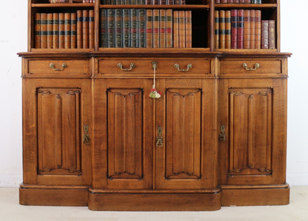 A large Victorian Gothic oak breakfront bookcase featuring open upper shelves filled with books and carved lower cupboard doors. View VI