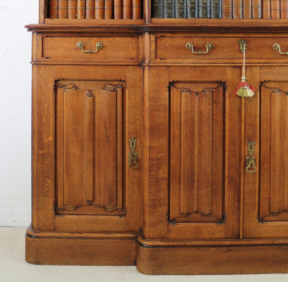 A large Victorian Gothic oak breakfront bookcase featuring open upper shelves filled with books and carved lower cupboard doors. View VII