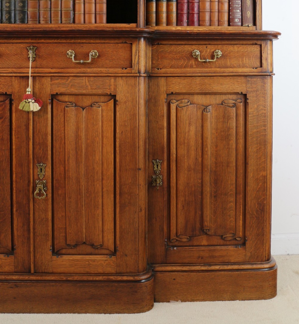 A large Victorian Gothic oak breakfront bookcase featuring open upper shelves filled with books and carved lower cupboard doors. View VIII