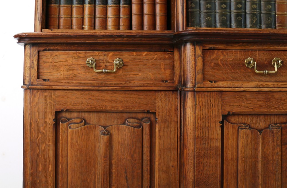 A large Victorian Gothic oak breakfront bookcase featuring open upper shelves filled with books and carved lower cupboard doors. View IX