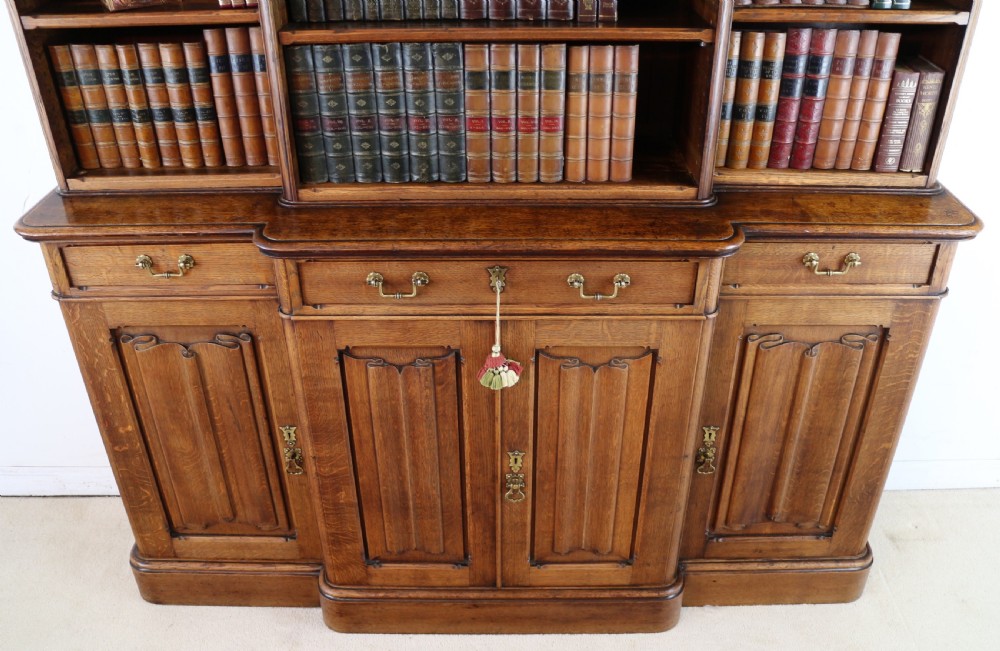 A large Victorian Gothic oak breakfront bookcase featuring open upper shelves filled with books and carved lower cupboard doors. View XII