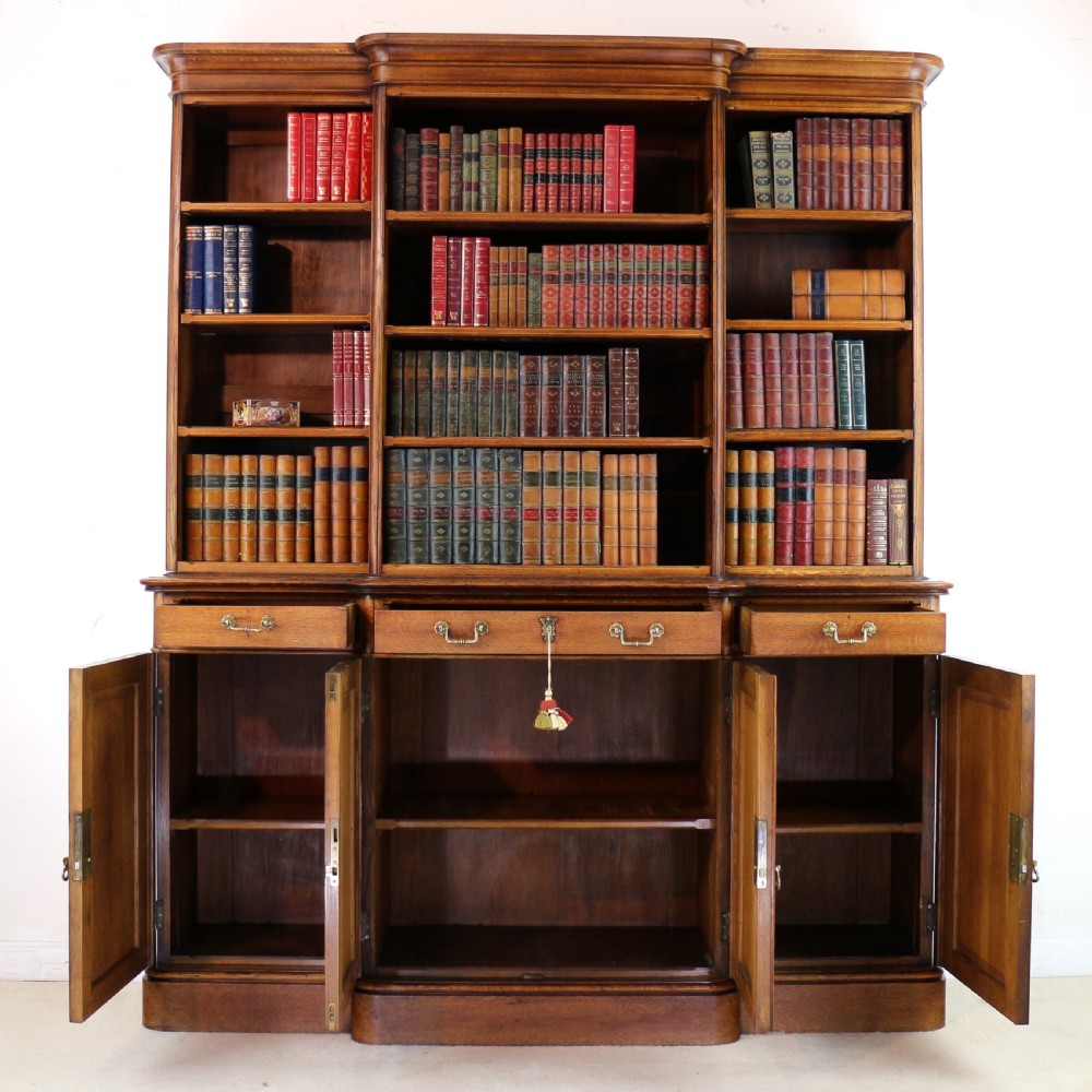 A large Victorian Gothic oak breakfront bookcase featuring open upper shelves filled with books and carved lower cupboard doors. View XV