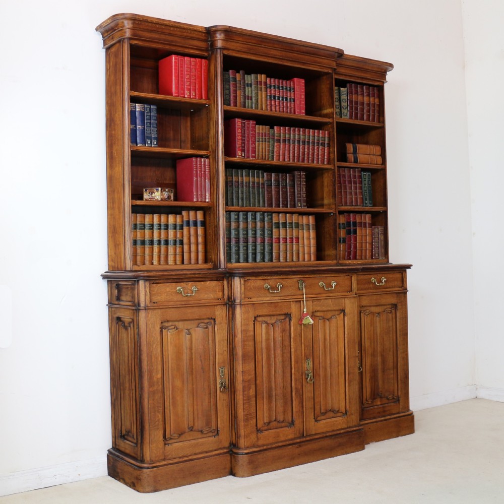 A large Victorian Gothic oak breakfront bookcase featuring open upper shelves filled with books and carved lower cupboard doors. View XIX
