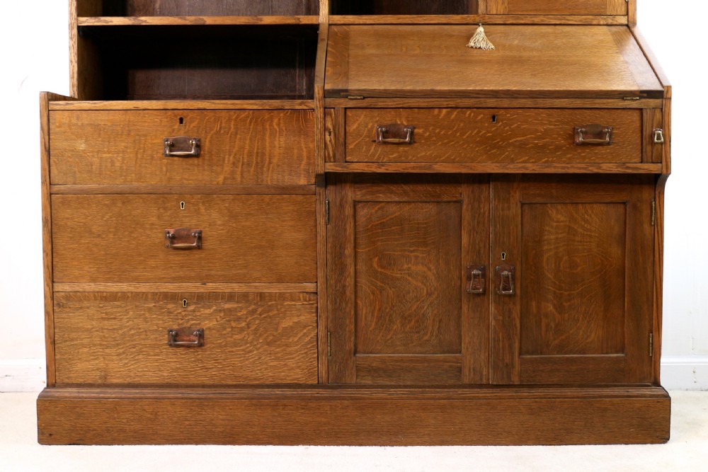 An Arts and Crafts quarter-sawn oak bureau bookcase featuring an asymmetrical design with open shelves, a fall-front writing slope, a leaded green glass cabinet, and drawers with copper handles. View III
