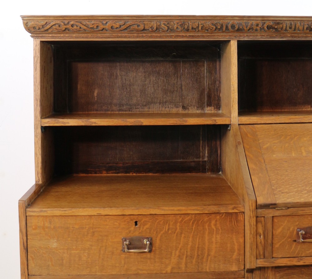 An Arts and Crafts quarter-sawn oak bureau bookcase featuring an asymmetrical design with open shelves, a fall-front writing slope, a leaded green glass cabinet, and drawers with copper handles. View V