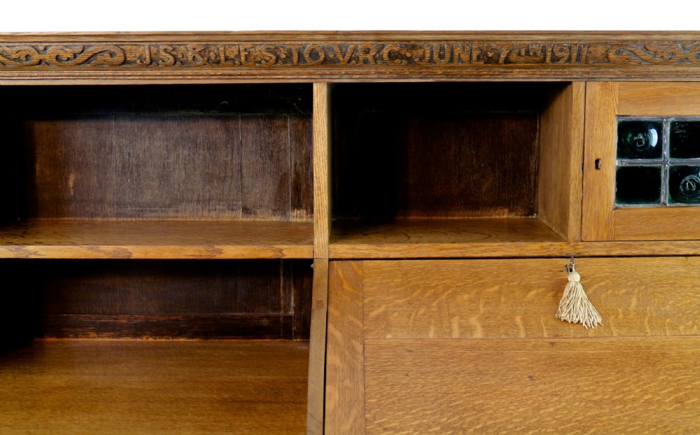 An Arts and Crafts quarter-sawn oak bureau bookcase featuring an asymmetrical design with open shelves, a fall-front writing slope, a leaded green glass cabinet, and drawers with copper handles. View VI