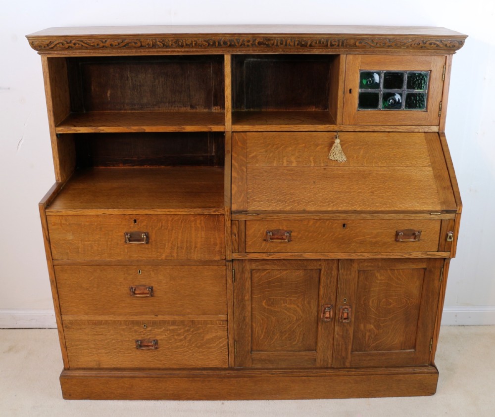 An Arts and Crafts quarter-sawn oak bureau bookcase featuring an asymmetrical design with open shelves, a fall-front writing slope, a leaded green glass cabinet, and drawers with copper handles. View VIII