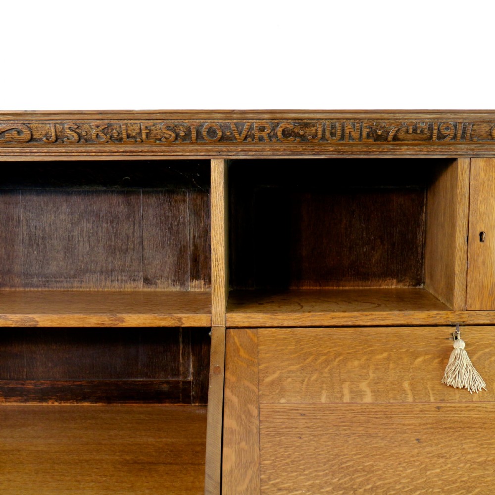 An Arts and Crafts quarter-sawn oak bureau bookcase featuring an asymmetrical design with open shelves, a fall-front writing slope, a leaded green glass cabinet, and drawers with copper handles. View IX