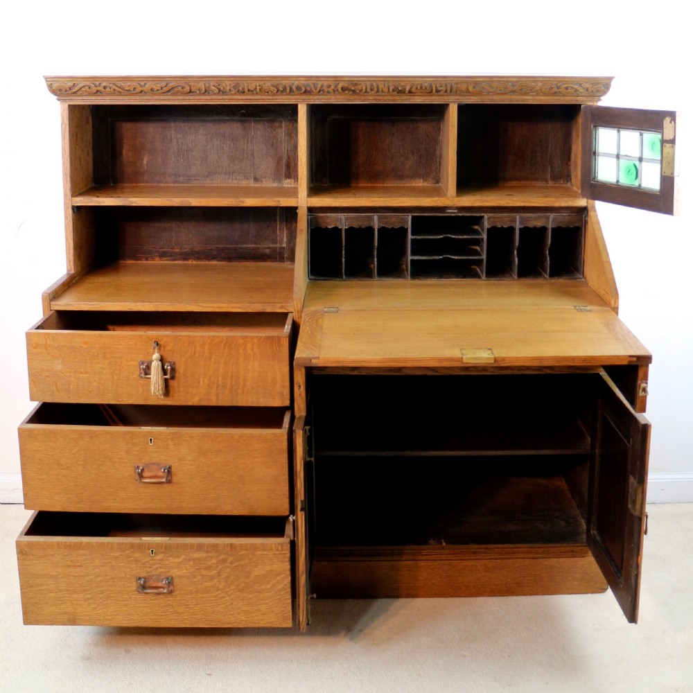 An Arts and Crafts quarter-sawn oak bureau bookcase featuring an asymmetrical design with open shelves, a fall-front writing slope, a leaded green glass cabinet, and drawers with copper handles. View XIII
