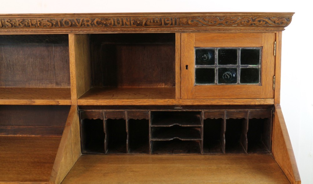 An Arts and Crafts quarter-sawn oak bureau bookcase featuring an asymmetrical design with open shelves, a fall-front writing slope, a leaded green glass cabinet, and drawers with copper handles. View XV