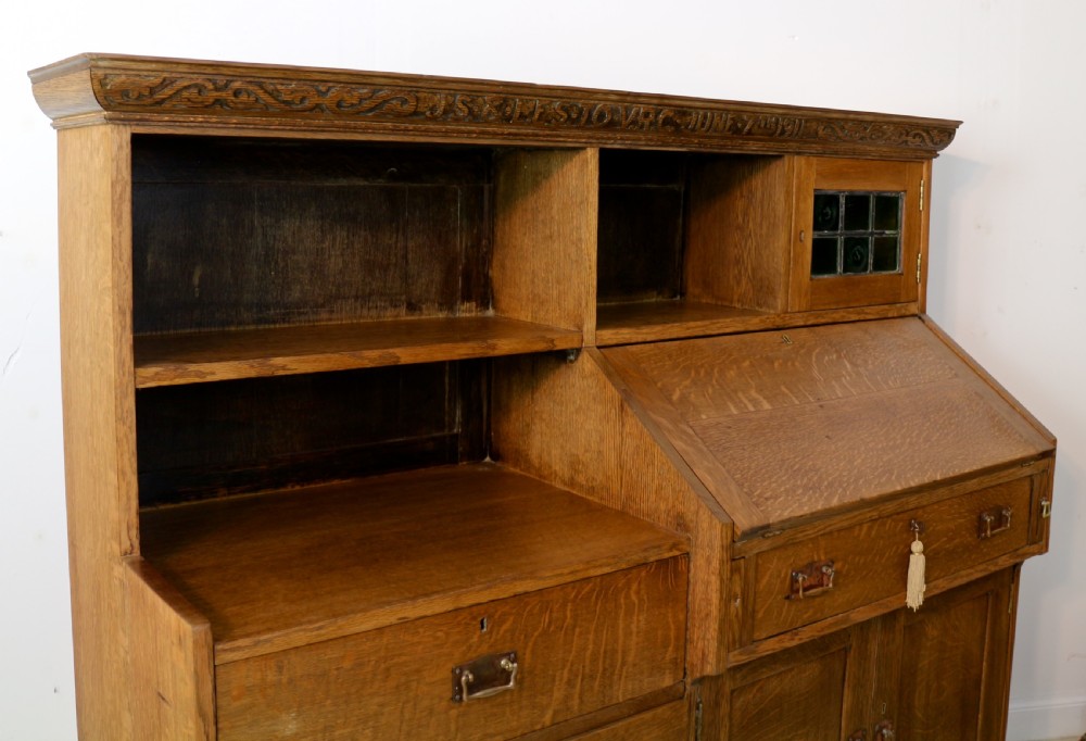 An Arts and Crafts quarter-sawn oak bureau bookcase featuring an asymmetrical design with open shelves, a fall-front writing slope, a leaded green glass cabinet, and drawers with copper handles. View XVIII