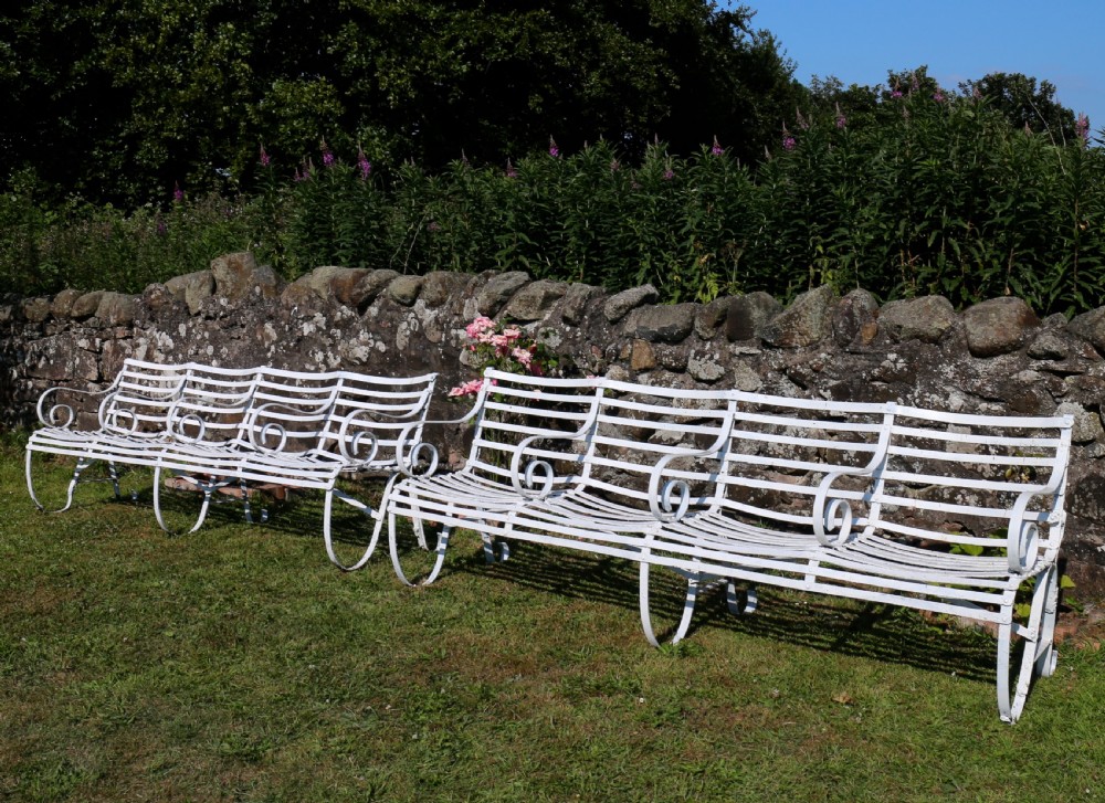 A pair of long white painted wrought iron Victorian garden benches with slatted backs and seats and scrolled armrests. View II