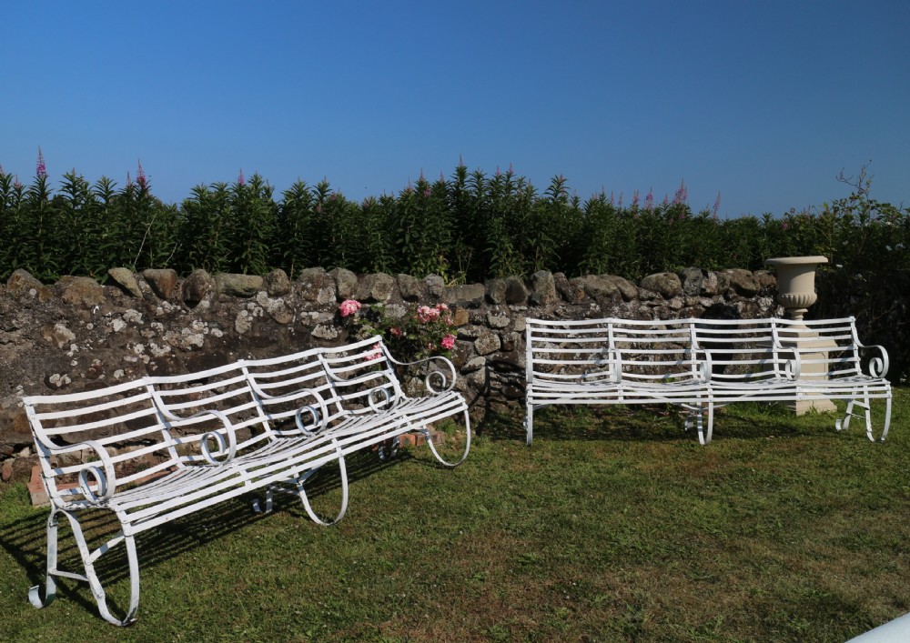A pair of long white painted wrought iron Victorian garden benches with slatted backs and seats and scrolled armrests. View III