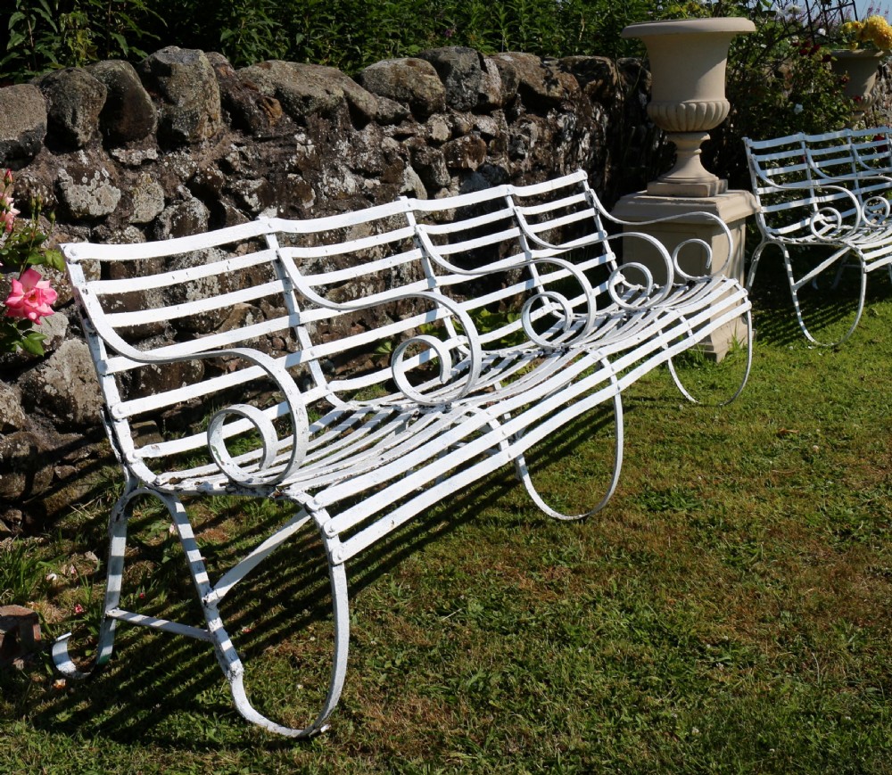 A pair of long white painted wrought iron Victorian garden benches with slatted backs and seats and scrolled armrests. View V