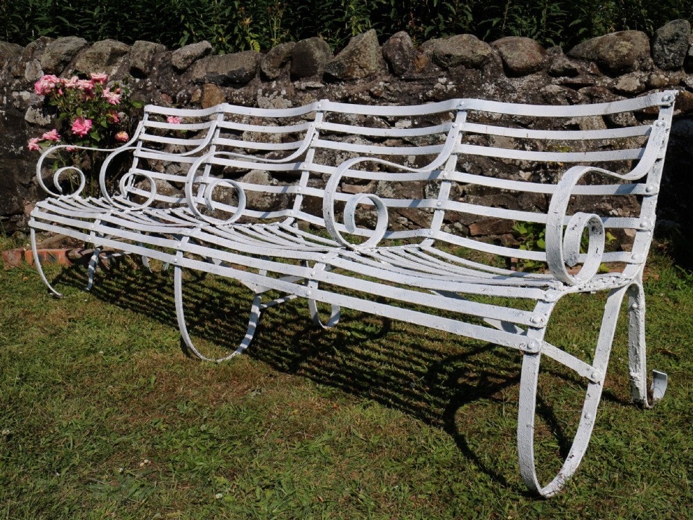 A pair of long white painted wrought iron Victorian garden benches with slatted backs and seats and scrolled armrests. View VI