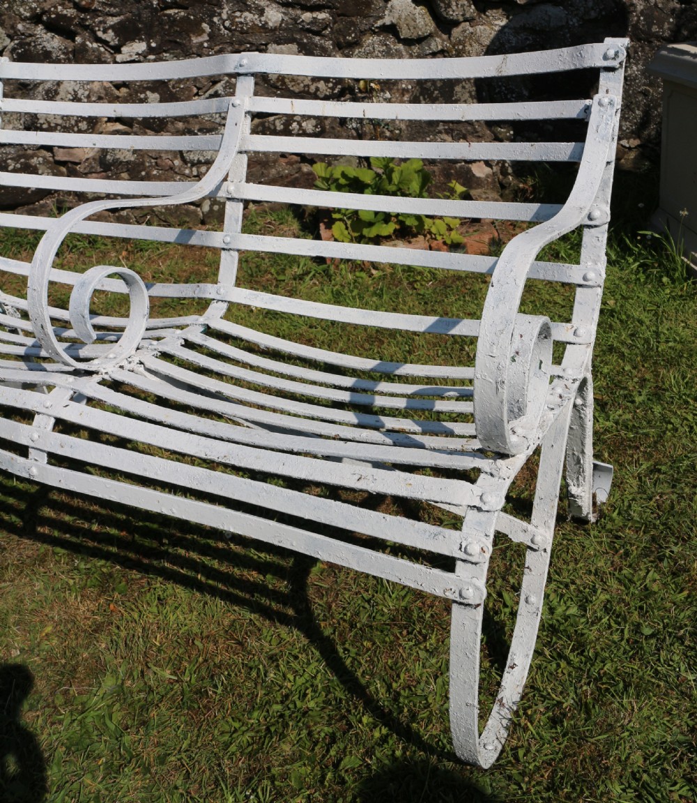A pair of long white painted wrought iron Victorian garden benches with slatted backs and seats and scrolled armrests. View XI