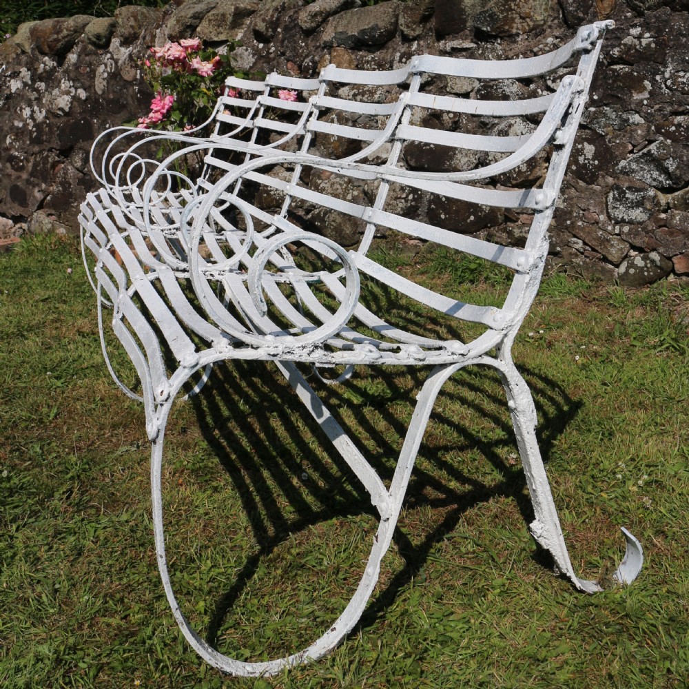 A pair of long white painted wrought iron Victorian garden benches with slatted backs and seats and scrolled armrests. View XII