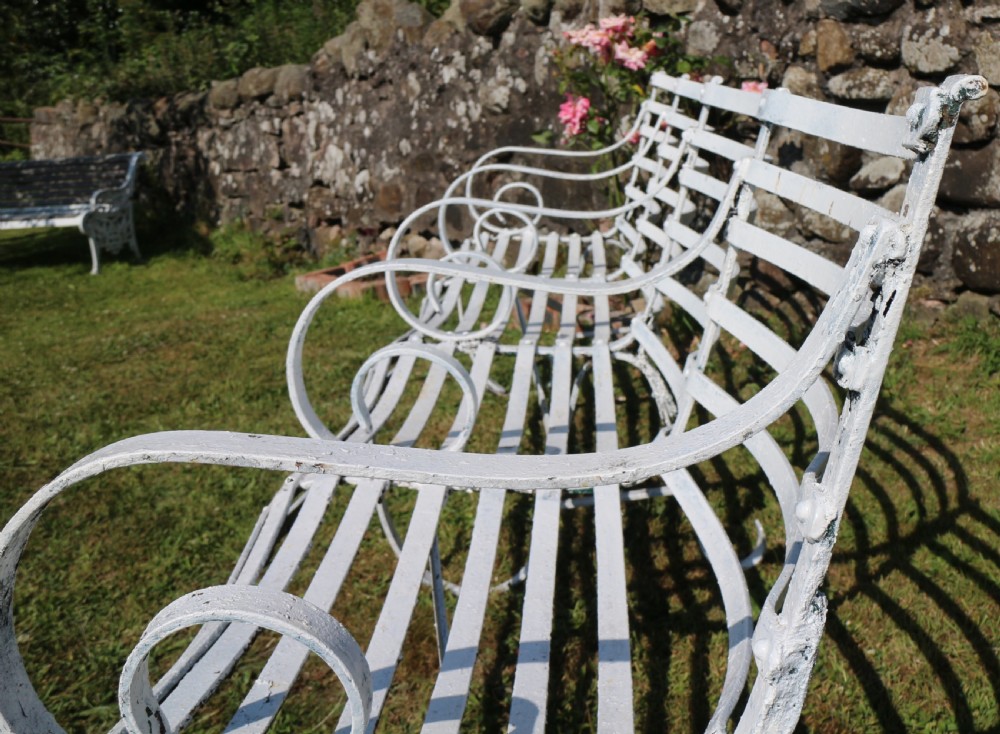 A pair of long white painted wrought iron Victorian garden benches with slatted backs and seats and scrolled armrests. View XV
