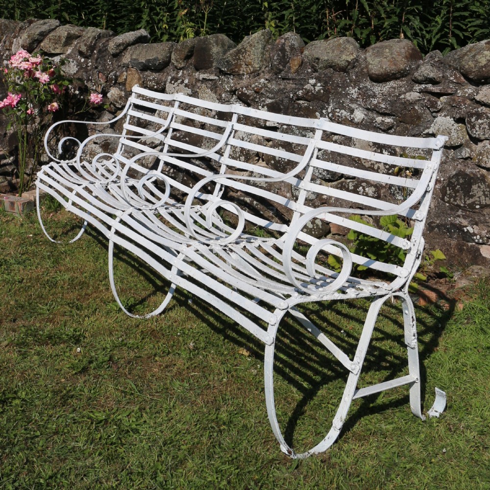 A pair of long white painted wrought iron Victorian garden benches with slatted backs and seats and scrolled armrests. View XVII