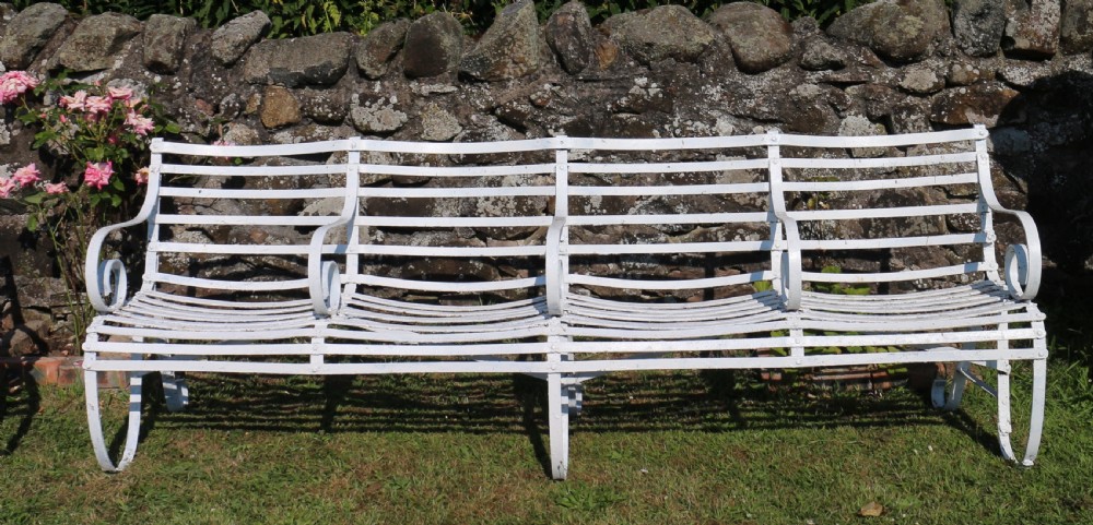 A pair of long white painted wrought iron Victorian garden benches with slatted backs and seats and scrolled armrests. View XVIII