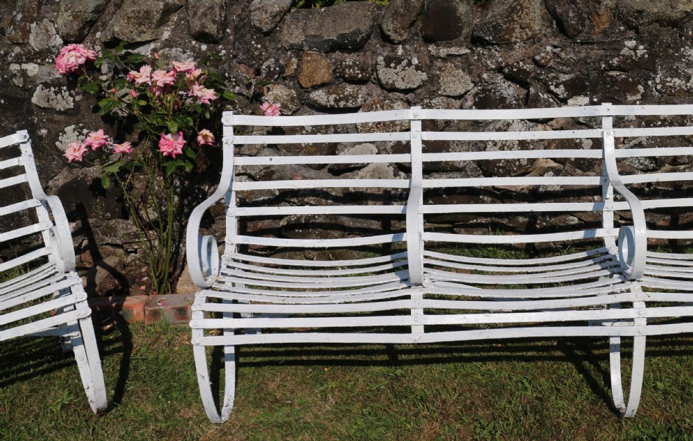 A pair of long white painted wrought iron Victorian garden benches with slatted backs and seats and scrolled armrests. View XIX