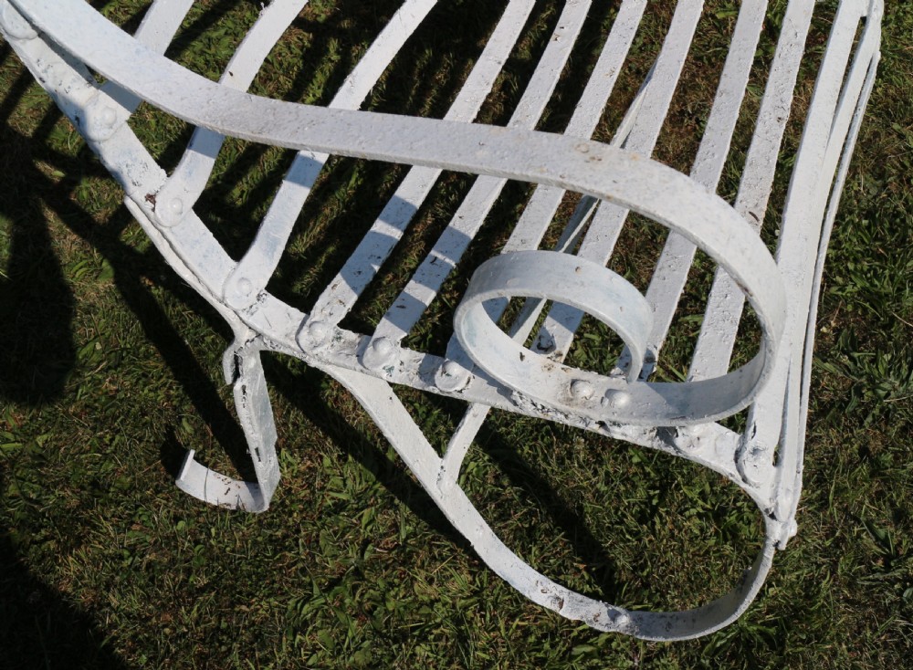 A pair of long white painted wrought iron Victorian garden benches with slatted backs and seats and scrolled armrests. View XXIV