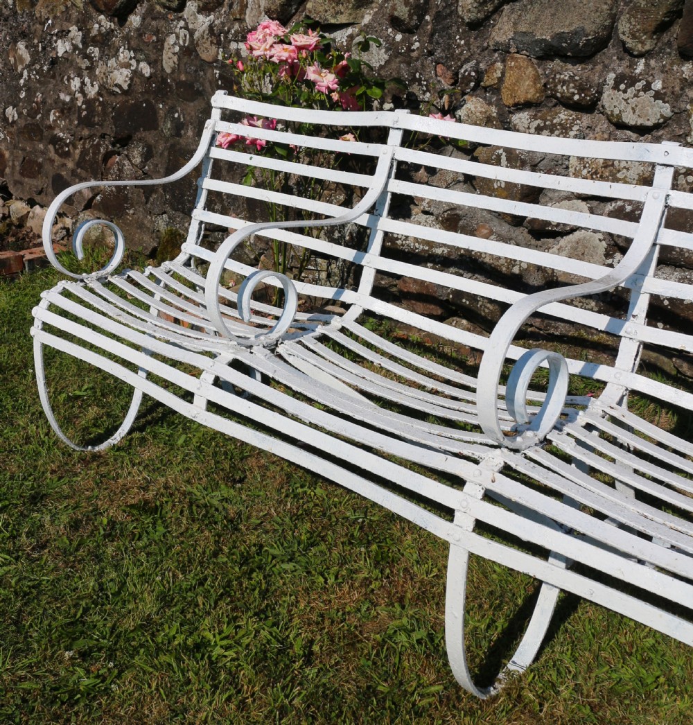 A pair of long white painted wrought iron Victorian garden benches with slatted backs and seats and scrolled armrests. View XXV