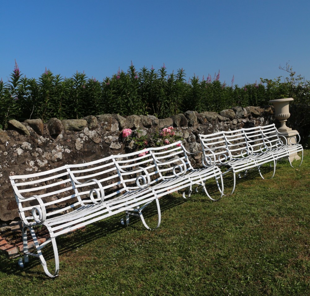 A pair of long white painted wrought iron Victorian garden benches with slatted backs and seats and scrolled armrests. View XXVII