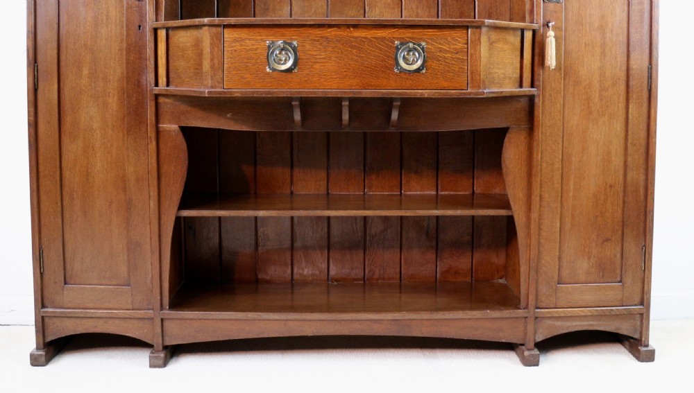 An Arts and Crafts solid oak sideboard featuring a central drawer, open shelving, and two side doors accented with green bullseye glass roundels. View V