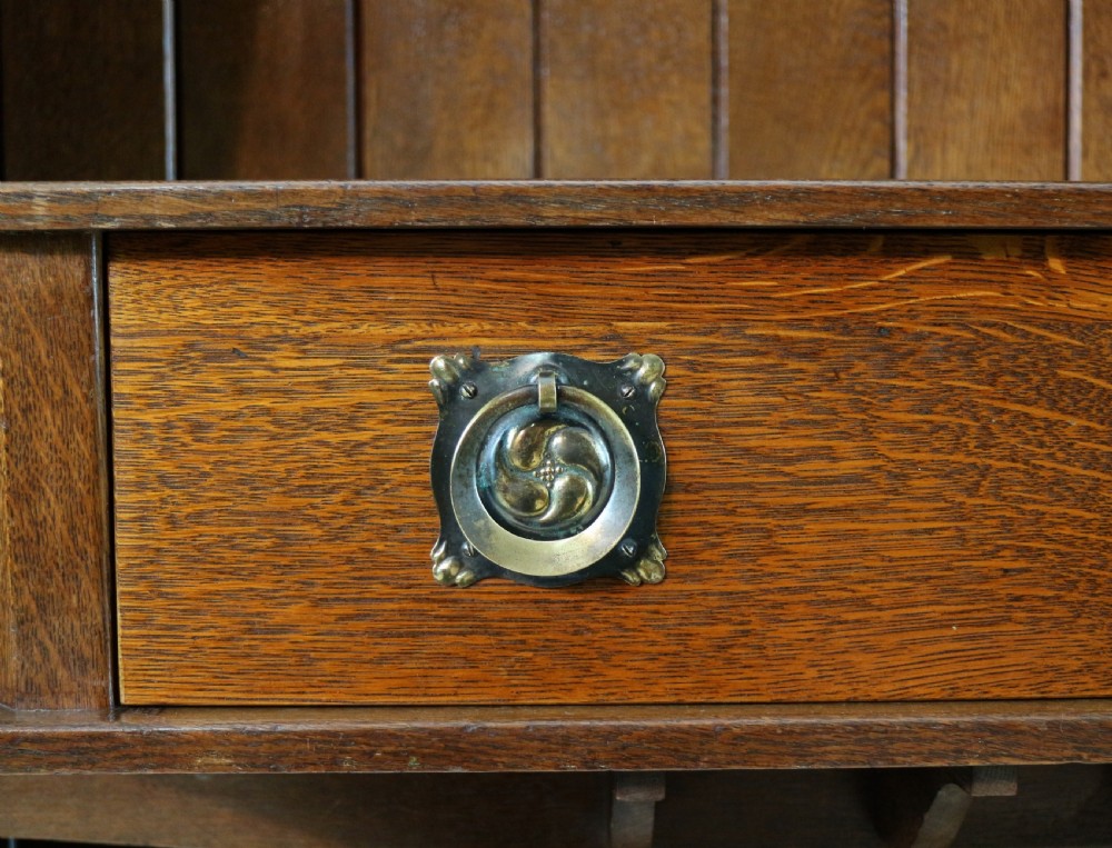 An Arts and Crafts solid oak sideboard featuring a central drawer, open shelving, and two side doors accented with green bullseye glass roundels. View VII