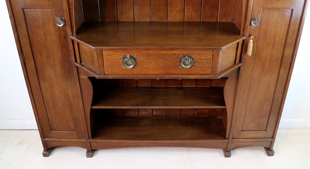 An Arts and Crafts solid oak sideboard featuring a central drawer, open shelving, and two side doors accented with green bullseye glass roundels. View VIII