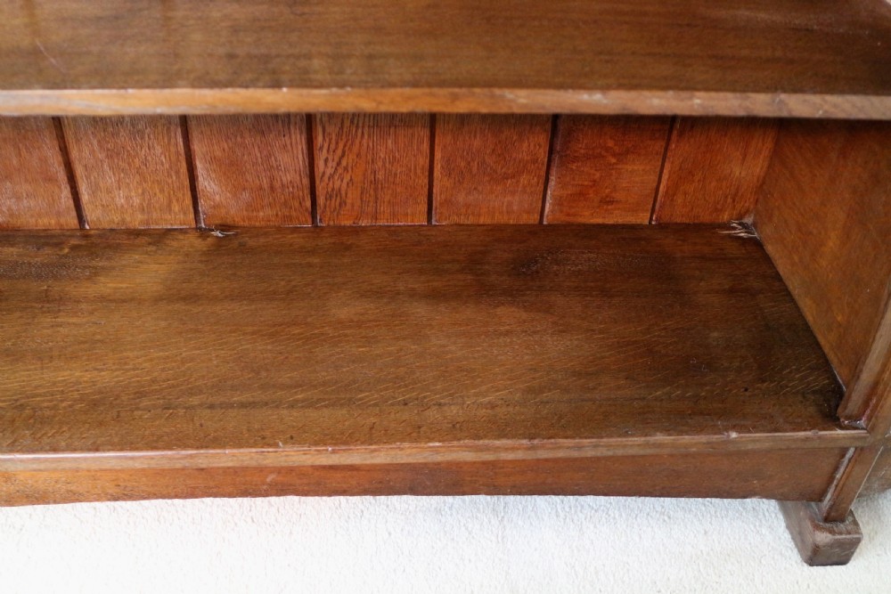 An Arts and Crafts solid oak sideboard featuring a central drawer, open shelving, and two side doors accented with green bullseye glass roundels. View XII