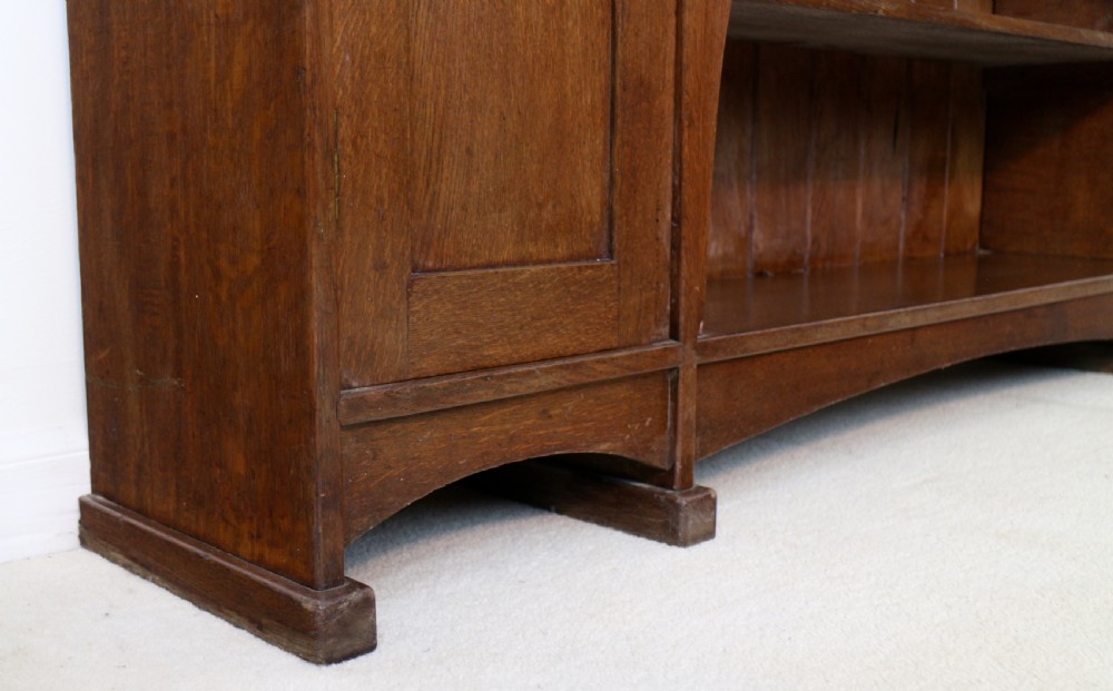 An Arts and Crafts solid oak sideboard featuring a central drawer, open shelving, and two side doors accented with green bullseye glass roundels. View XVIII