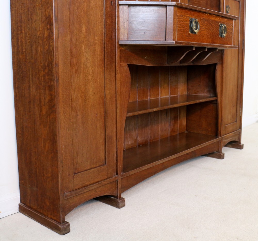 An Arts and Crafts solid oak sideboard featuring a central drawer, open shelving, and two side doors accented with green bullseye glass roundels. View XIX