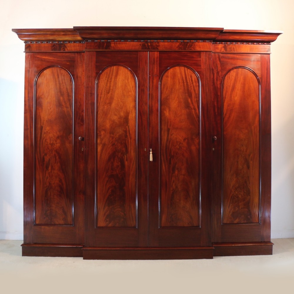 A nineteenth-century breakfront wardrobe featuring flame mahogany veneer, four arched panel doors, and a moulded projecting cornice.