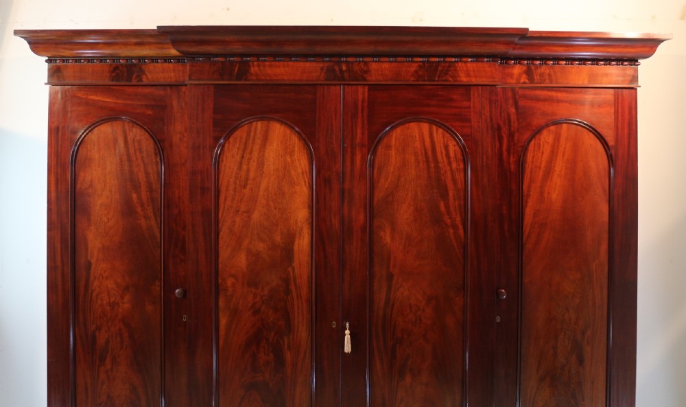 A nineteenth-century breakfront wardrobe featuring flame mahogany veneer, four arched panel doors, and a moulded projecting cornice. View III