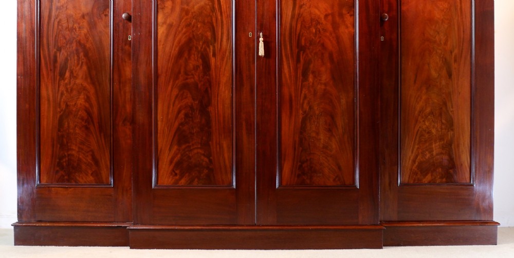 A nineteenth-century breakfront wardrobe featuring flame mahogany veneer, four arched panel doors, and a moulded projecting cornice. View VI