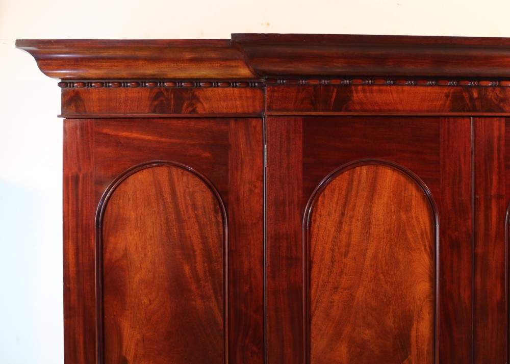 A nineteenth-century breakfront wardrobe featuring flame mahogany veneer, four arched panel doors, and a moulded projecting cornice. View VIII