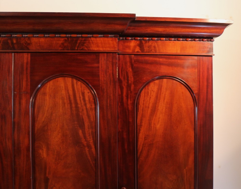 A nineteenth-century breakfront wardrobe featuring flame mahogany veneer, four arched panel doors, and a moulded projecting cornice. View IX