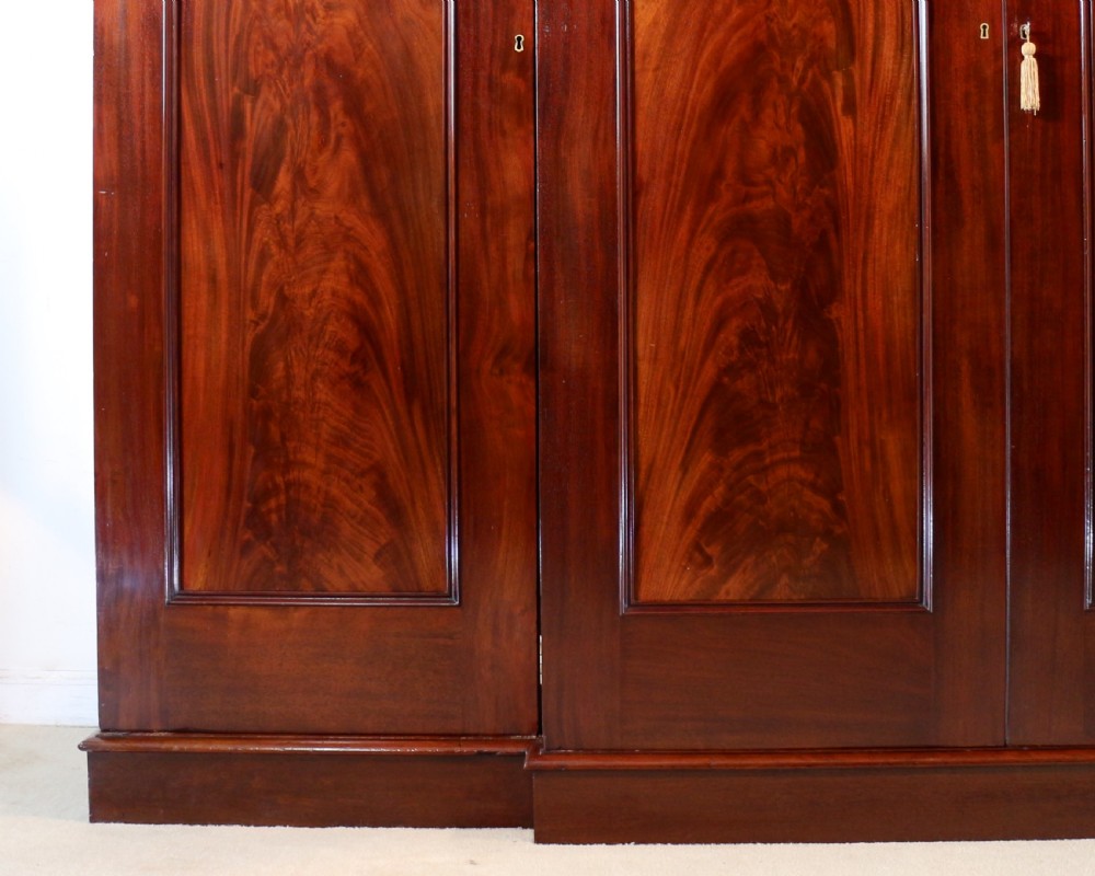 A nineteenth-century breakfront wardrobe featuring flame mahogany veneer, four arched panel doors, and a moulded projecting cornice. View X
