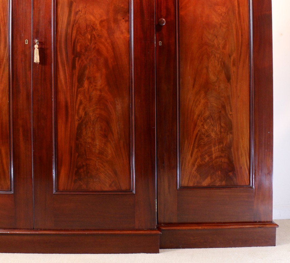 A nineteenth-century breakfront wardrobe featuring flame mahogany veneer, four arched panel doors, and a moulded projecting cornice. View XI