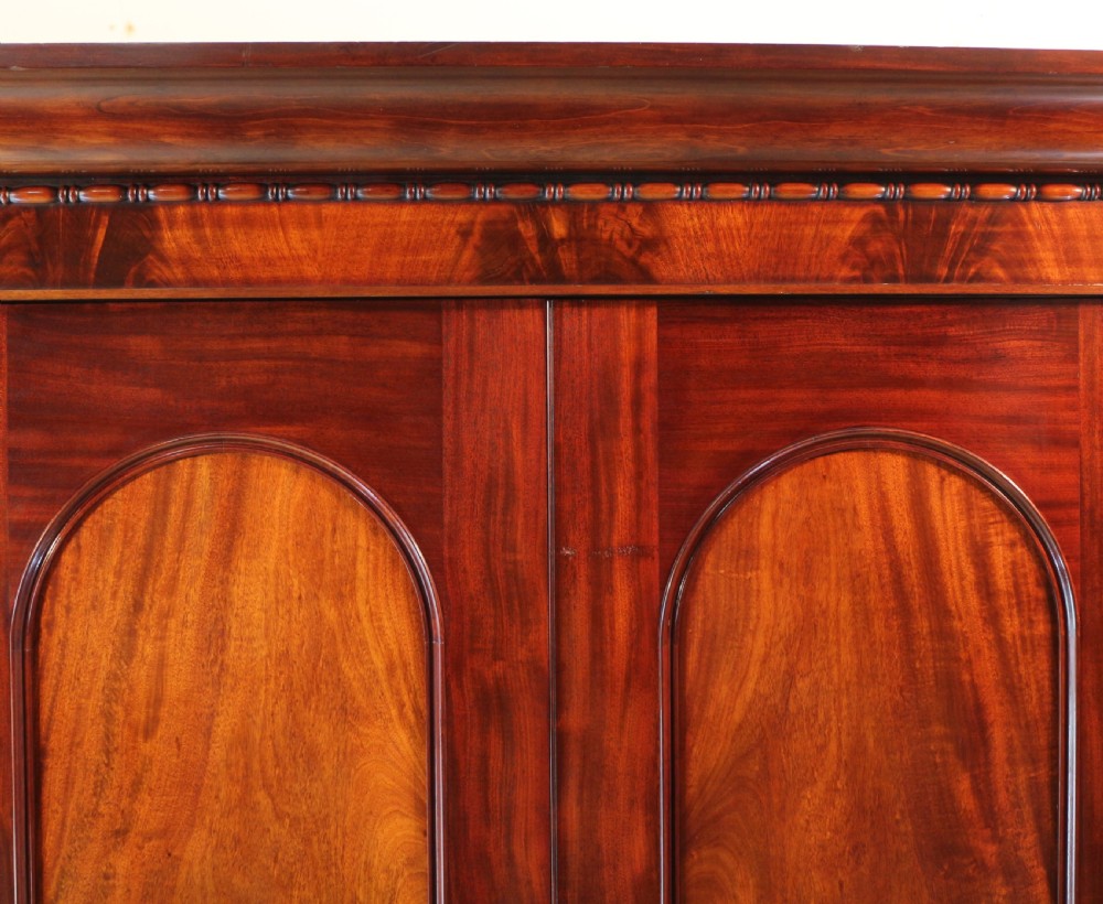 A nineteenth-century breakfront wardrobe featuring flame mahogany veneer, four arched panel doors, and a moulded projecting cornice. View XIII