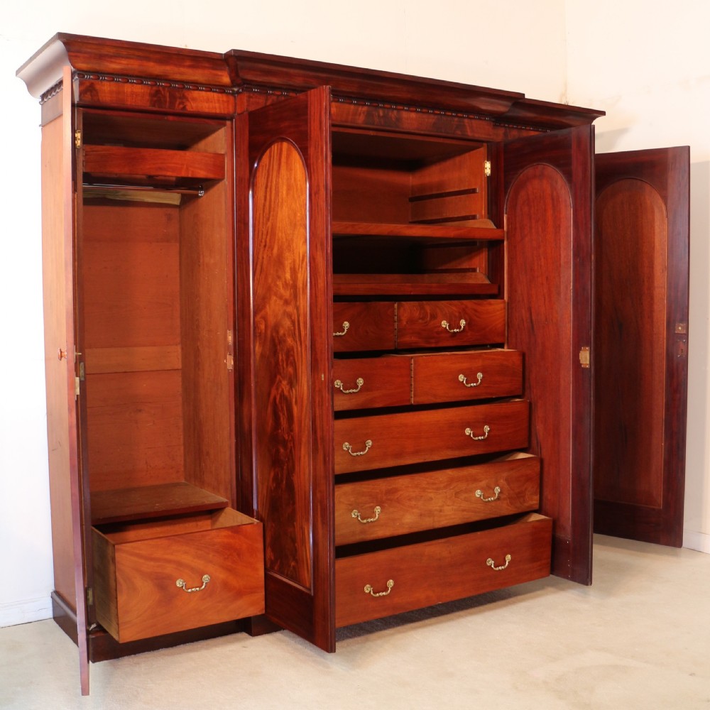A nineteenth-century breakfront wardrobe featuring flame mahogany veneer, four arched panel doors, and a moulded projecting cornice. View XIV