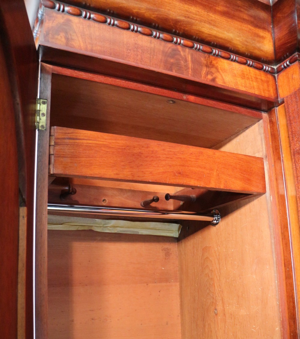 A nineteenth-century breakfront wardrobe featuring flame mahogany veneer, four arched panel doors, and a moulded projecting cornice. View XV