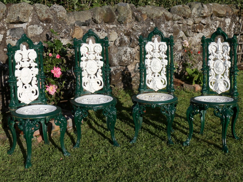 A set of four Victorian cast iron garden chairs featuring white openwork backrests with central medallion cameos framed by dark green structural frames and cabriole legs. View II