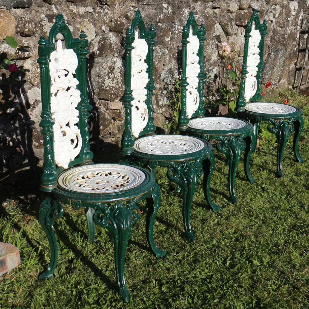 A set of four Victorian cast iron garden chairs featuring white openwork backrests with central medallion cameos framed by dark green structural frames and cabriole legs. View III
